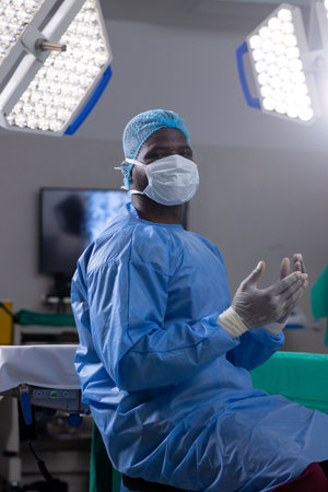 Portrait of african american male doctor with face mask and gloves in hospital operating room....
