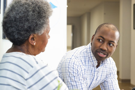 African american male doctor talking with senior woman in hospital waiting room. Medicine,...