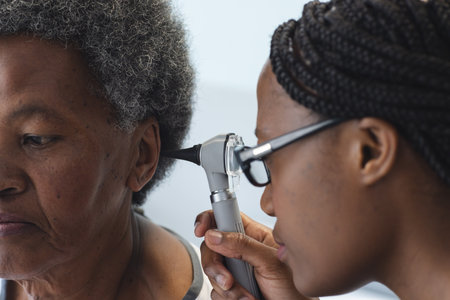 African american female doctor testing ear of senior female patient in hospital room. Medicine,...