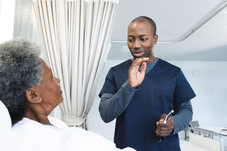 African american male doctor talking with senior female patient in hospital room. Medicine, healthcare and medical services, unaltered.の写真素材