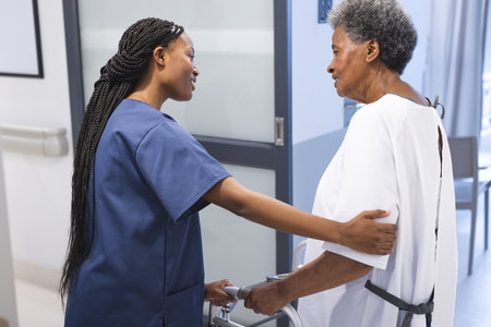 African american female doctor talking with senior female patient with crutches in hospital corridor. Medicine, healthcare and medical services, unaltered.の写真素材