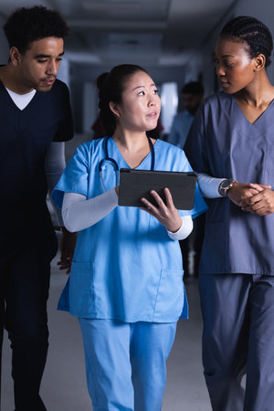 Diverse male and female doctors talking and using tablet walking in hospital corridor. Medicine,...