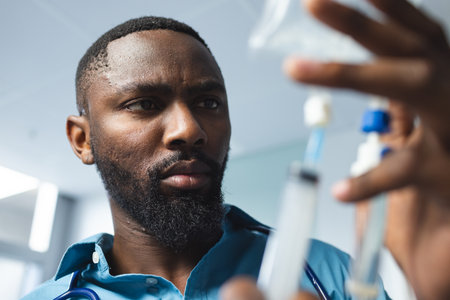 African american male doctor wearing blue shirt applying drip in hospital room. Medicine, healthcare, work and hospital, unaltered.の写真素材