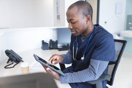 African american male doctor using tablet at reception desk in hospital. Medicine, healthcare,...