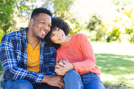Happy african american couple embracing and holding hands on stairs in sunny garden, copy space. Outdoors, expression, gesticulation, love, togetherness and nature, unaltered.の写真素材
