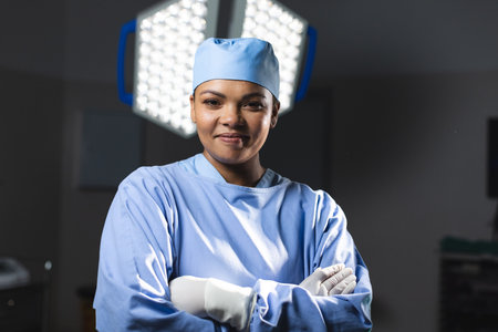 Portrait of happy biracial female surgeon wearing surgical gown in operating theatre. Medicine, healthcare, surgery, work and hospital, unaltered.の写真素材