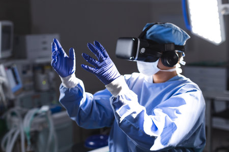Biracial female surgeon wearing surgical gown using vr headset in operating theatre. Medicine, healthcare, surgery, technology, work and hospital, unaltered.の写真素材