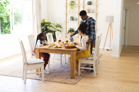 Happy african american man pouring tea to cup at breakfast in morning at home, copy space. Togetherness, parenthood, childhood, food and drink, domestic life and healthy lifestyle, unaltered.の写真素材