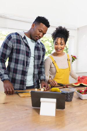 Happy african american couple preparing fresh snack from fruits in kitchen at home, copy space. Togetherness, food and drink, domestic life and healthy lifestyle, unaltered.の写真素材