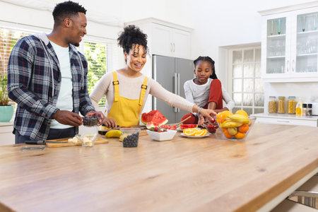 Happy african american family preparing fresh snack from fruits in kitchen at home, copy space. Togetherness, parenthood, childhood, food and drink, domestic life and healthy lifestyle, unaltered.の写真素材