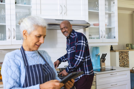 Diverse senior couple preparing meal using tablet in kitchen. Lifestyle, retirement, senior lifestyle, food, cooking, togetherness, communication, recipe and domestic life, unaltered.の写真素材