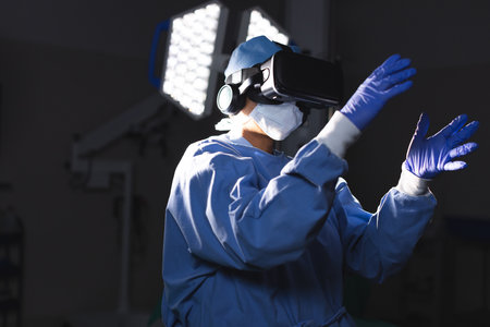 Biracial female surgeon wearing surgical gown using vr headset in operating theatre. Medicine, healthcare, surgery, technology, work and hospital, unaltered.の写真素材