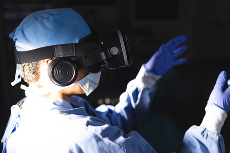 Biracial female surgeon wearing surgical gown using vr headset in operating theatre. Medicine, healthcare, surgery, technology, work and hospital, unaltered.の写真素材