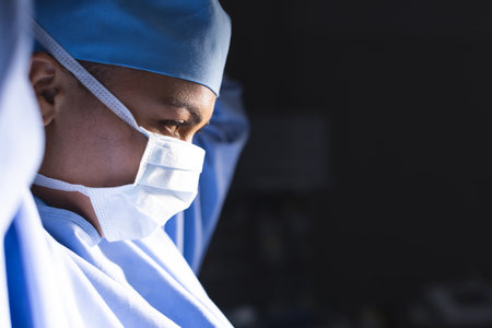 Biracial female surgeon wearing surgical gown and face mask in operating theatre, copy space. Medicine, healthcare, surgery, work and hospital, unaltered.の写真素材