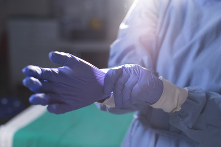 Midsection of biracial female surgeon wearing surgical gown and medical gloves in operating theatre. Medicine, healthcare, surgery, work and hospital.の写真素材