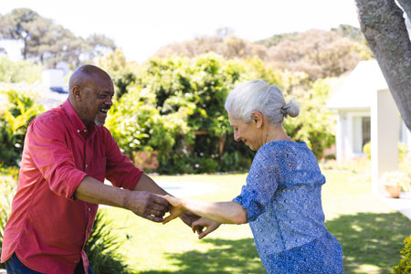 Happy diverse senior couple dancing in sunny garden. Lifestyle, retirement, senior lifestyle, nature, togetherness and domestic life, unaltered.の写真素材