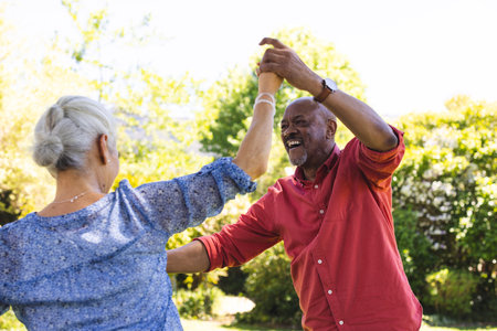 Happy diverse senior couple dancing in sunny garden. Lifestyle, retirement, senior lifestyle, nature, togetherness and domestic life, unaltered.の写真素材
