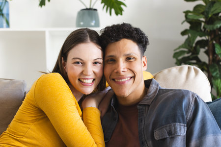 Happy diverse couple sitting on couch and embracing in living room at home, copy space. Expression,...