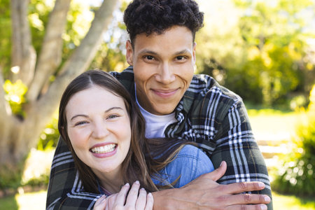 Portrait of happy diverse couple embracing in sunny garden, copy space. Outdoors, expression, love, togetherness and nature unaltered.の写真素材