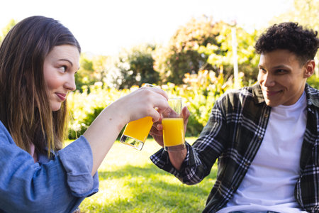 Happy diverse couple sitting on making a toast in sunny garden, copy space. Outdoors, expression, leisure, love, togetherness, food and drink and nature unaltered.の写真素材
