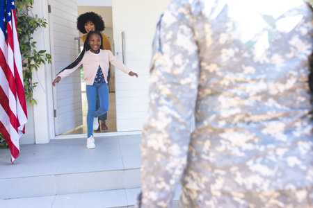 Happy african american wife and daughter welcoming male soldier outdoors with usa flag, copy space. Expression, togetherness, military, army, protection, duty, patriotism and nationality, unaltered.の写真素材