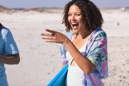 Young biracial woman laughs joyfully at the beach. Her vibrant expression adds life to this sunny...