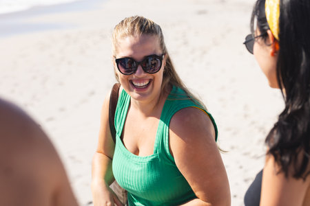 Young Caucasian woman enjoys a sunny beach day with friends. Outdoor leisure time is captured as she shares a laugh in a casual setting.の写真素材