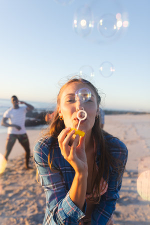 Young Caucasian woman blows bubbles on a sunny beach. Outdoor leisure activity captures a joyful...