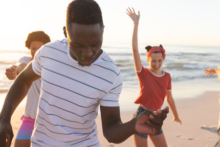 Friends enjoy a playful moment on the beach. The diverse group creates a vibrant, joyful outdoor scene.の写真素材