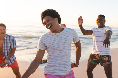 Diverse friends enjoy a beach outing. Laughter and joy fill the air as they play by the seaside at sunset.の写真素材