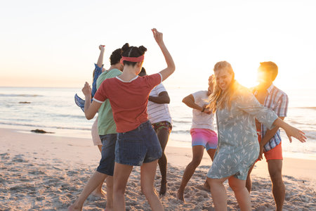 Diverse group of friends dance on the beach at sunset. Laughter and joy fill the air as they celebrate the day's end outdoors.の写真素材
