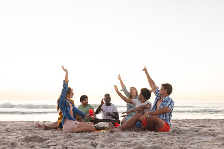 Diverse group of friends enjoy a beach sunset and having a party, with copy space. Laughter and high-fives create a relaxed outdoor atmosphere.の写真素材