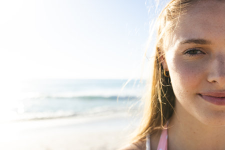 Close-up of a young Caucasian woman at the beach, with copy space. Sunlight enhances her serene...