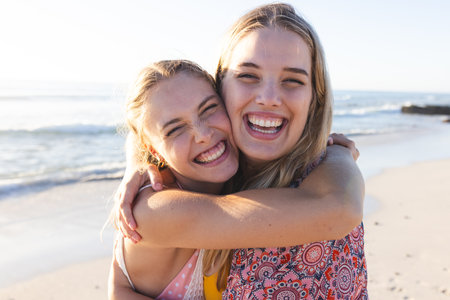 Caucasian young female friends embracing on a sunny beach. Their laughter and closeness capture a...