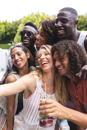 Diverse group of friends share a joyful moment, embracing and laughing together. Outdoor setting enhances the casual, happy vibe as they enjoy a sunny day.の写真素材
