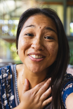 Portrait of happy asian woman with long hair having video call at home. Domestic life, technology and lifestyle, unaltered.の写真素材