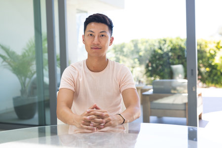Young Asian man seated at a modern home office on a video call. His confident posture suggests a professional setting or a business meeting.の写真素材