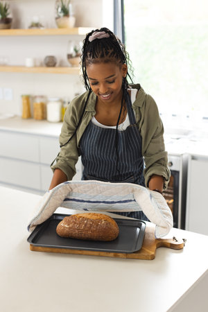 African American young woman checking freshly baked bread. She has braided hair, wearing casual...
