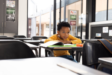 African American boy sits in a school classroom, his expression pensive, with copy space. Surrounded...