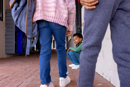 African American boy sits crouched between other children in school, looking sad. His gaze is directed upwards, capturing a moment of curiosity or concern amidst an urban setting.の写真素材