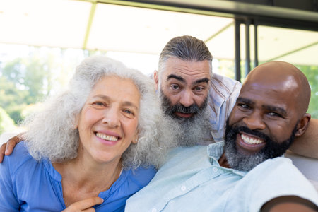 Diverse senior friends, Caucasian and African American, smile at home. Wearing casual clothes, enjoying warmth and sharing laughter under sunny sky, unalteredの写真素材