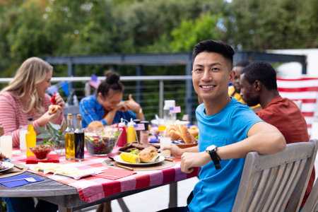 Portrait of happy diverse group of friends talking and having dinner at balcony with flags of usa. Independence day, tradition, friendship, patriotism, food and lifestyle, unaltered.の写真素材