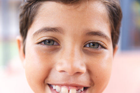 In school, young biracial male student is smiling at the camera outdoors. He has light brown skin, dark brown hair, and hazel eyes, unaltered.の写真素材