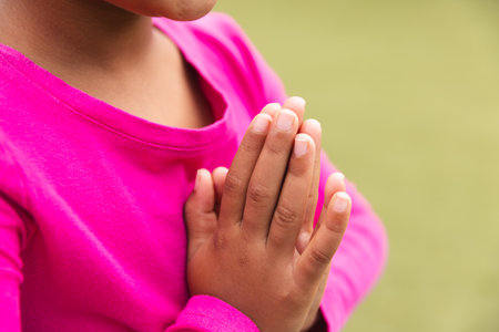 In school, young biracial female student wearing a bright pink top is praying outdoors and doing...