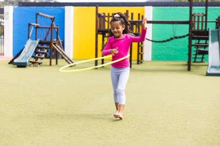In school playground outdoors, biracial young girl playing with ring hoop. She wearing pink top, gray leggings, barefoot, hair tied back, unalteredの写真素材