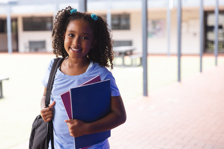 Biracial girl smiling at school, with copy space. She's ready for a day of learning with books in hand.の写真素材