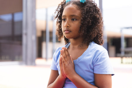 Biracial girl praying outdoors, with copy space. Captured moment reflects a sense of hope or spirituality in a school setting.の写真素材