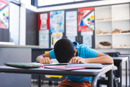 Biracial boy studying intently in a classroom at school. He is focused on writing in his notebook during a lesson.の写真素材