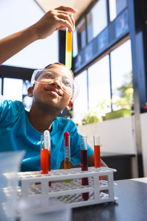 Biracial boy examines a test tube in a school lab classroom. His curiosity shines as he engages in a hands-on science experiment.の写真素材