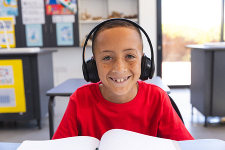 Biracial boy studies in a classroom at school on a video call. He's focused on his schoolwork while...